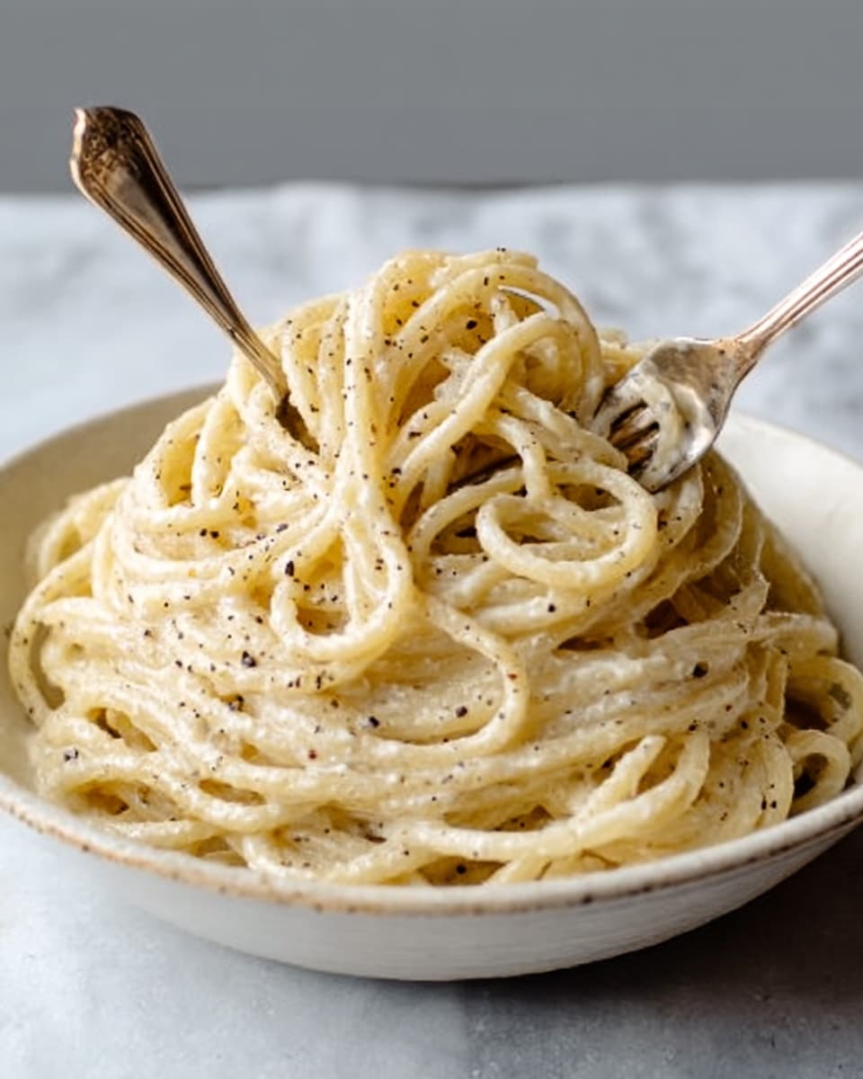 A white bowl filled with creamy pasta noodles, light yellow in color with a smooth texture, layered in a swirled mound. The top is sprinkled with grated white cheese, adding a slightly grainy look, and a woman's hand holds a fork twirling some noodles near the edge. The bowl sits on a white marbled surface, with soft natural light from above. photo taken with an iphone --ar 4:5 --v 7