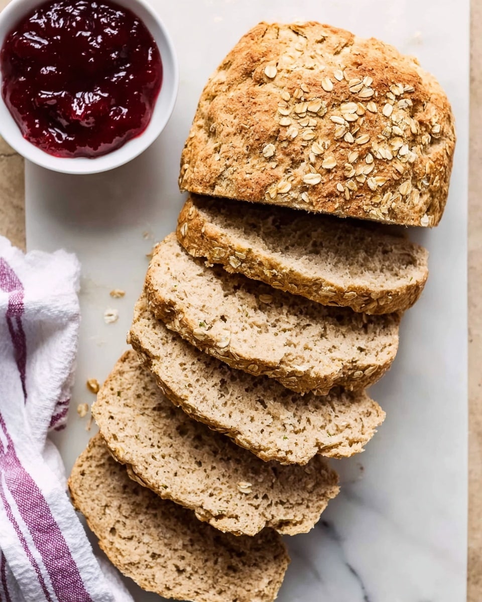 The image shows a loaf of oat bread sliced into five pieces, placed on a white marbled surface. The bread has a rough texture with visible oats on the top crust, which is golden brown in color. Each slice reveals a soft, dense inside with a light brown hue and small air pockets. To the top left of the bread, there is a white bowl filled with dark red jam, adding a bright contrast to the image. A woman's hand with a white and purple striped cloth is seen touching the bread from the bottom left corner. Photo taken with an iphone --ar 4:5 --v 7