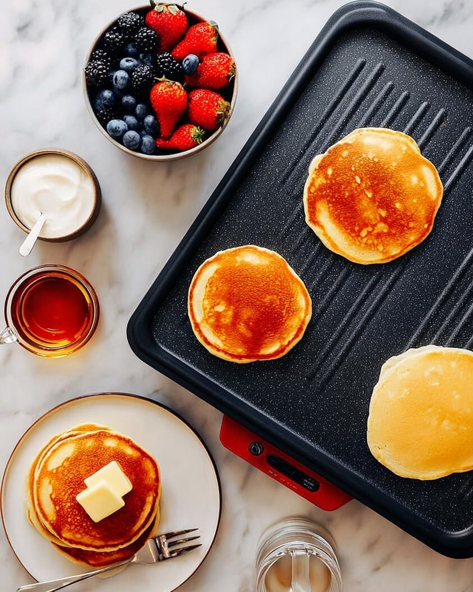 The image shows a black electric griddle with four pancakes cooking on it; three pancakes are golden brown and one pancake is still pale and uncooked at the bottom. On the left side, there is a small white bowl with white cream, a small glass cup with amber syrup, and a white plate with a stack of two golden brown pancakes, topped with a square of butter and a few blueberries. A silver fork rests on the plate. Above these, there is a white bowl filled with fresh strawberries, blueberries, and blackberries. All items are placed on a white marbled surface. photo taken with an iphone --ar 4:5 --v 7