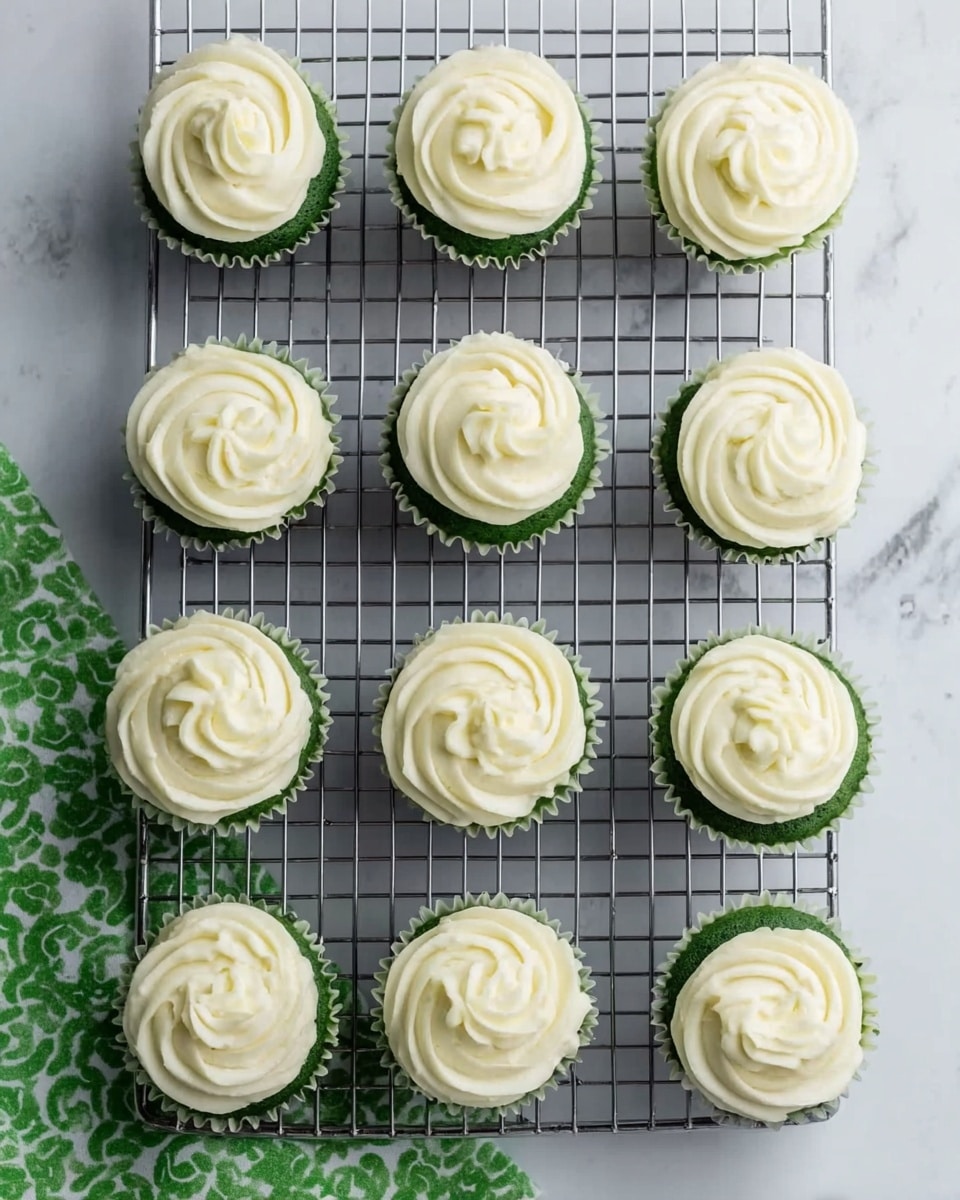 The image shows twelve green cupcakes arranged in four rows of three on a cooling rack, placed on a white marbled surface. Each cupcake has a swirl of creamy white frosting on top with a smooth, slightly ridged texture, evenly spread in a spiral pattern. The green cake base is visible at the bottom of each cupcake, contrasting with the white frosting above. In the lower corner, a piece of green and white patterned cloth is partially visible. photo taken with an iphone --ar 4:5 --v 7