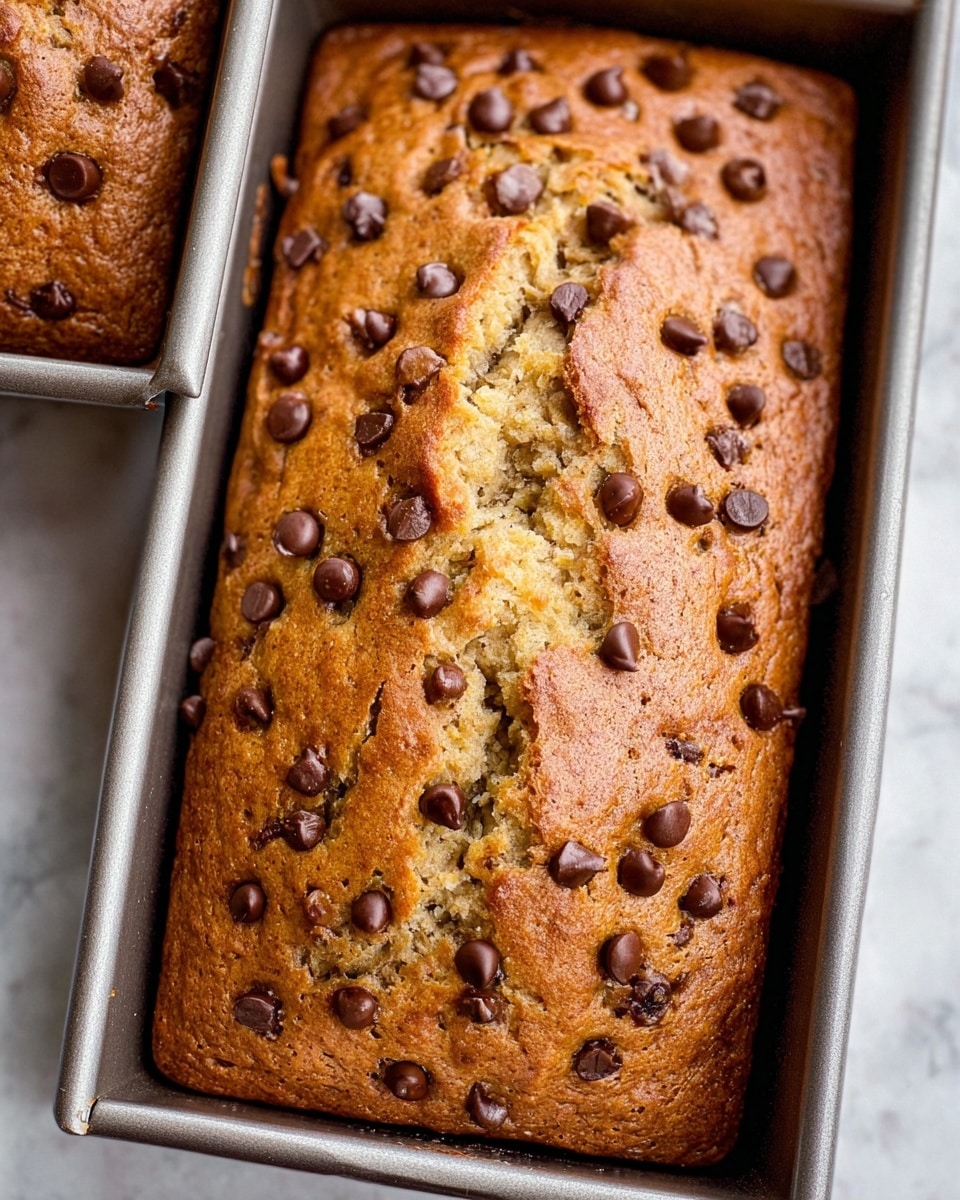 The image shows two golden-brown rectangular loaves of chocolate chip bread resting on a black cooling rack, placed on a white marbled surface covered with a white cloth that has thin black lines. The bread loaves have a slightly cracked texture on the top and are dotted with melted chocolate chips spread unevenly across the surface. Some loose chocolate chips are scattered around the loaves. To the right, a small white cup filled with light brown coffee or tea completes the warm, inviting scene. photo taken with an iphone --ar 4:5 --v 7