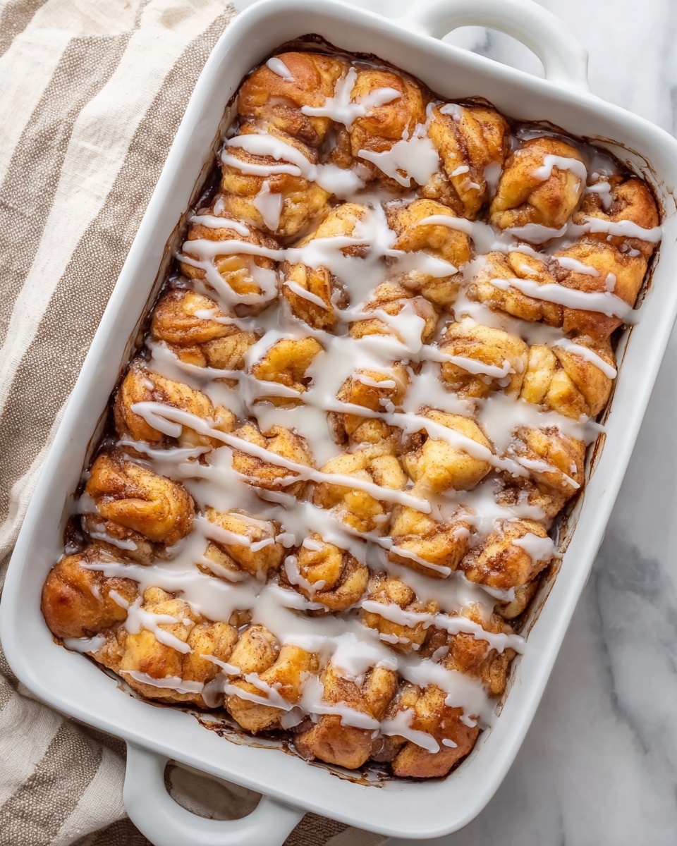 The image shows a white rectangular baking dish filled with a baked dessert made of many small dough pieces, each golden brown with a soft and fluffy texture. The dough pieces are closely packed together in a slightly raised layer. A white glaze is drizzled unevenly over the entire surface, creating thin lines that contrast with the warm brown color of the dough. The dish is placed on a white marbled surface next to a beige and white striped cloth. Photo taken with an iphone --ar 4:5 --v 7