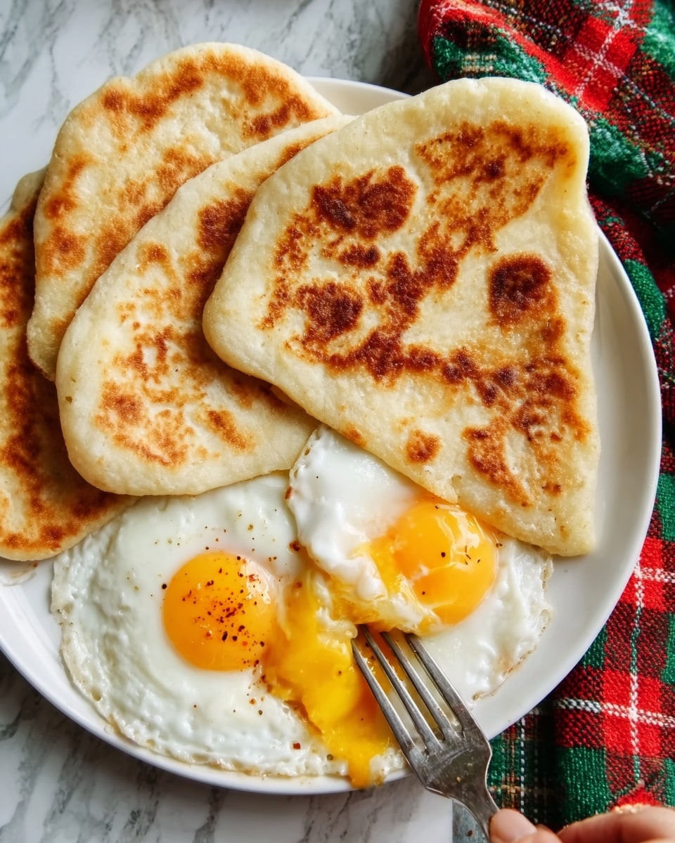 A white plate on a white marbled surface holds three pieces of golden-brown pita bread arranged in a triangle shape. Next to the bread, there are two fried eggs with bright yellow yolks slightly broken, showing their runny texture. A woman's hand holding a fork is about to take a bite from the eggs. A red and green checkered cloth is partially visible in the background. Photo taken with an iphone --ar 4:5 --v 7