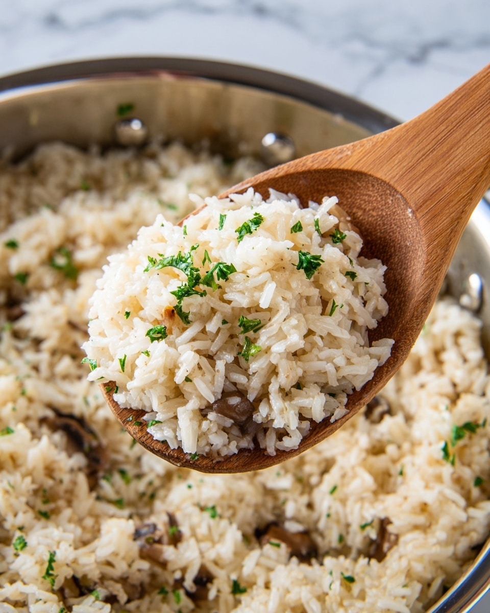 A close-up view shows a wooden spoon lifting a scoop of soft white rice mixed with small bits of brown mushrooms and sprinkled with tiny green parsley leaves. The rice looks fluffy and slightly shiny, with each grain separate but tender. The background is a shiny metal pan filled with more of the same rice mixture, and the setting rests on a white marbled surface. The lighting is natural, making the colors bright and inviting. photo taken with an iphone --ar 4:5 --v 7