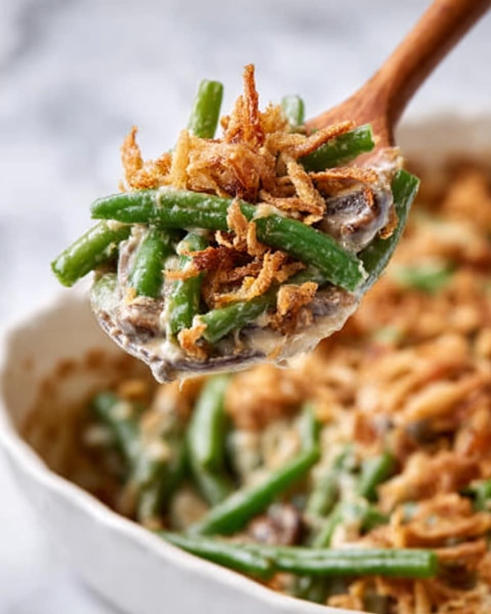 A close-up shot shows a wooden spoon lifting a serving of creamy green bean casserole. The spoon holds green beans covered with a smooth, light-colored creamy sauce. On top of the green beans, there are small, crispy, light brown fried onions scattered, adding texture and color contrast. The spoon is above a white dish filled with more of the same green bean casserole. The background is a white marbled surface. Photo taken with an iphone --ar 4:5 --v 7