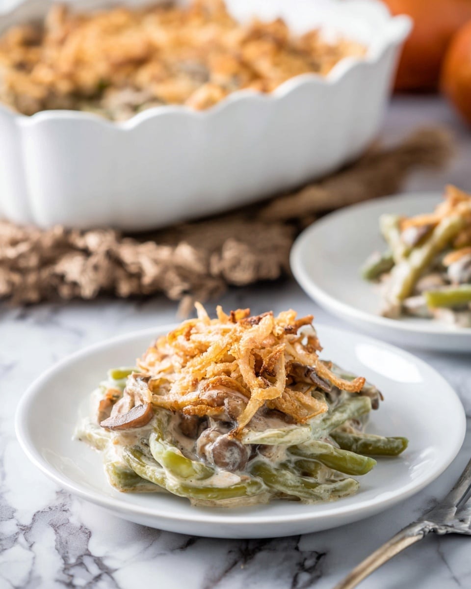 A serving of creamy green bean casserole sits on a small white plate in the front, showing three main layers: a soft green bean layer at the bottom mixed with creamy white sauce, a middle layer of tender mushrooms and sauce, topped with a crunchy golden-brown fried onion layer. Behind it, a white baking dish with more casserole and another plate is slightly out of focus. The surface beneath everything is a white marbled texture. Photo taken with an iphone --ar 4:5 --v 7