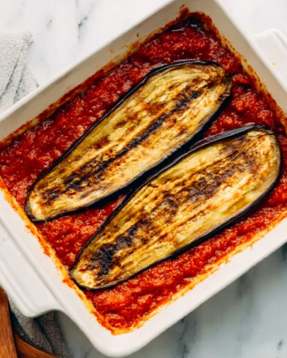 The dish shows two long, thin, golden-brown slices of grilled eggplant placed side by side on top of a thick red tomato sauce in a white rectangular ceramic dish. The eggplant has dark grill marks and a slightly wrinkled texture, giving a roasted look. The tomato sauce beneath is somewhat chunky and bright red, filling the base of the dish evenly. The dish sits on a white marbled surface with part of a wooden utensil visible in the corner. Photo taken with an iphone --ar 4:5 --v 7