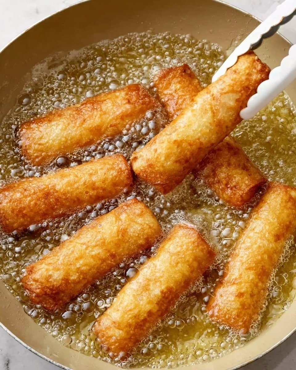The image shows seven golden brown roll-shaped snacks frying in hot bubbling oil inside a light-colored pan. One roll is held with white tongs, slightly lifted above the oil, showing its crispy and textured surface. The oil bubbles around the rolls appear lively and clear, highlighting the frying process. The background is a white marbled texture. Photo taken with an iphone --ar 4:5 --v 7