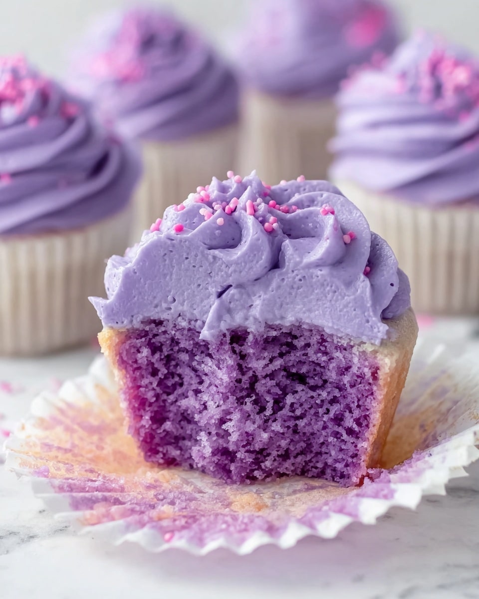 A close-up view of a purple cupcake with two layers; the bottom layer is the soft purple cake wrapped in a white paper liner, and the top layer is a tall, swirled, smooth lavender frosting with a creamy texture, sprinkled with small purple sugar crystals. A white and purple striped paper straw is placed standing inside the frosting on the right side. The cupcake sits on a white marbled surface scattered with more purple sugar. In the background, there is a purple soda can and additional purple frosted cupcakes out of focus. Photo taken with an iphone --ar 4:5 --v 7