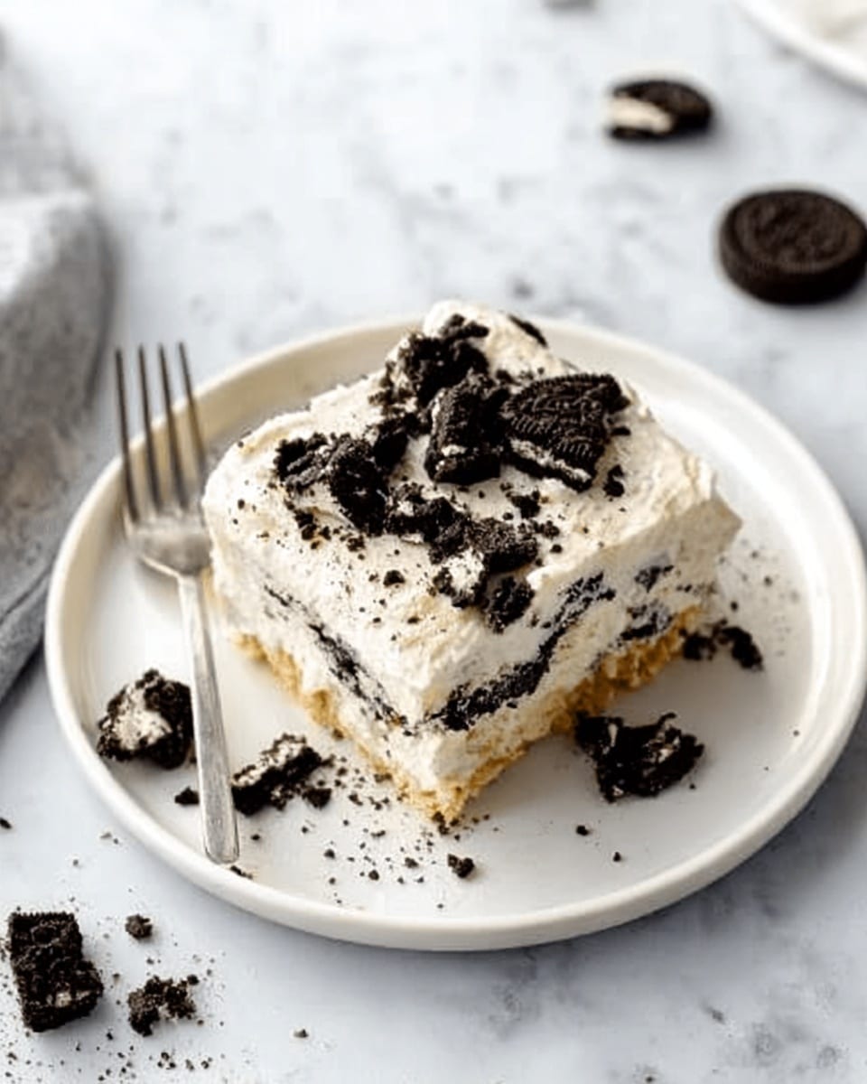 A square piece of creamy dessert on a white plate sits on a white marbled surface. The dessert has three layers: the bottom layer is light and crumbly, the middle layer is smooth and white, and the top layer is thick white cream with crushed dark cookie pieces sprinkled all over. Some cookie chunks are also scattered on the plate around the dessert. A woman’s hand holds a fork near the plate, ready to take a bite. Photo taken with an iphone --ar 4:5 --v 7
