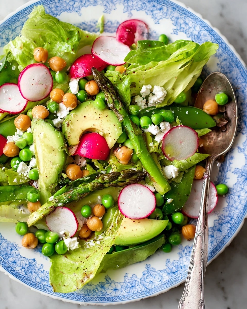The image shows a fresh vegetable salad on a white plate with blue patterns on the rim, placed on a white marbled surface. The salad has many layers including green lettuce leaves as the base, scattered with bright green peas and wedges of light green avocado. There are slices of pink and white radish layered on top, along with vibrant red radishes. Light brown chickpeas add a crunchy texture throughout the salad, while green asparagus pieces lay across the top. Small white crumbles of cheese are sprinkled over everything. A silver spoon rests on the plate’s edge, partly covered by the salad. Photo taken with an iphone --ar 4:5 --v 7