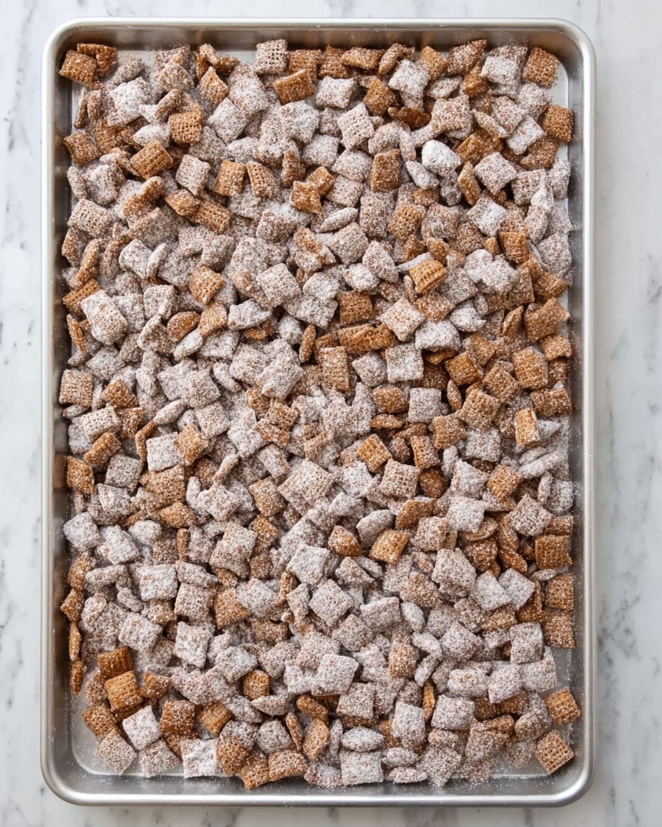 A large metal baking tray filled to the edges with many small, square-shaped snack pieces coated in white powdered sugar, showing a mix of lighter and darker brown pieces spread evenly across the tray. The tray is set on a white marbled surface, highlighting the contrast between the light powder and the brown snack pieces. photo taken with an iphone --ar 4:5 --v 7
