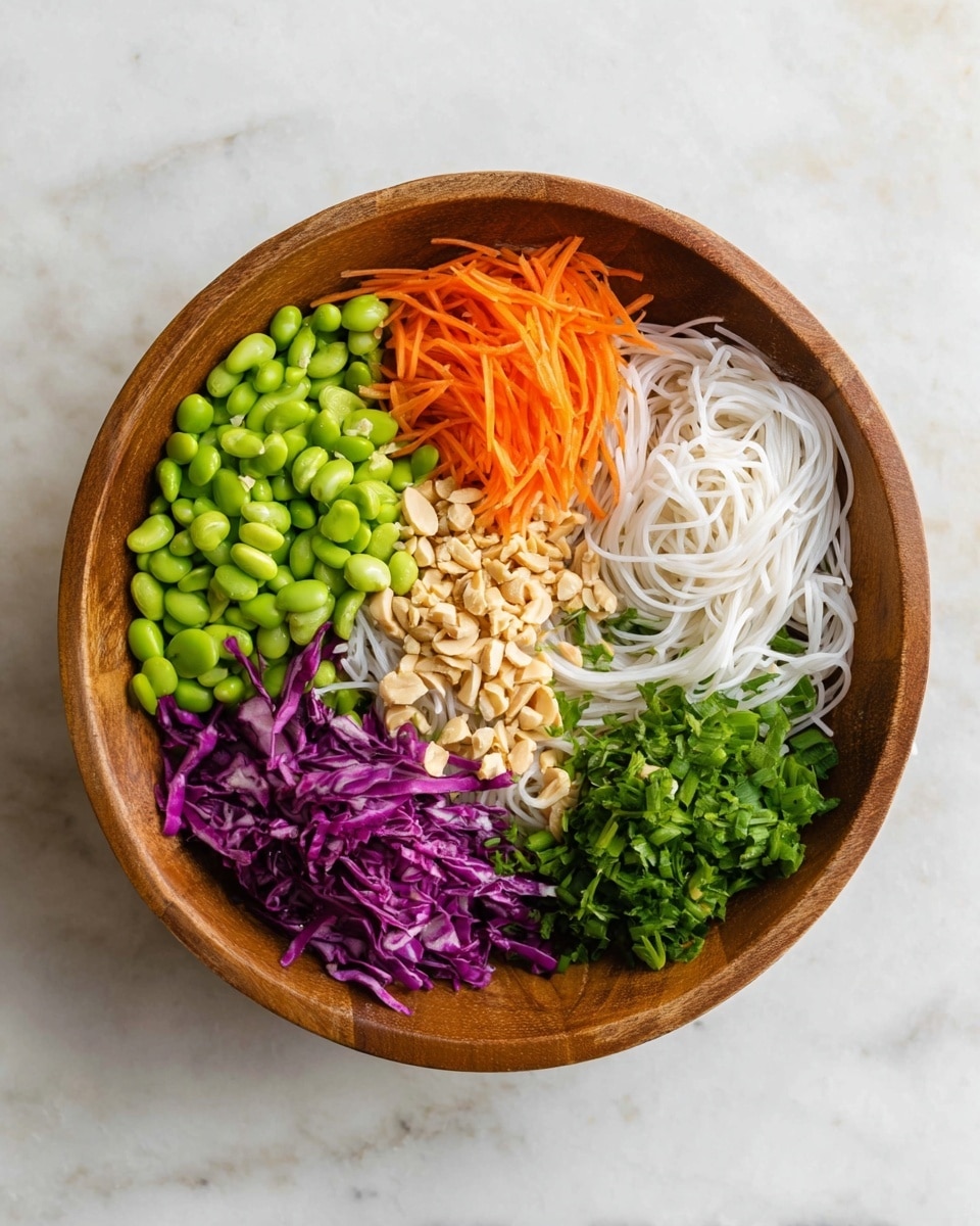 A wooden bowl contains six layers each in separate sections: bright green edamame beans at the top, thin orange carrot strips on the top right, chopped green leafy herbs on the bottom right, a bundle of white rice noodles at the bottom center, finely chopped green onions on the bottom left, and shredded purple cabbage on the top left. In the middle, there is a small pile of chopped light brown nuts. The bowl rests on a white marbled surface. photo taken with an iphone --ar 4:5 --v 7