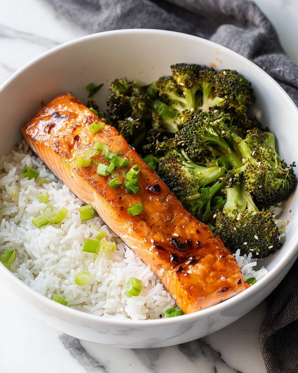 A white bowl filled with three layers: at the bottom, fluffy white rice with small bright green chopped scallions scattered on top; in the middle, a long piece of glazed salmon with a shiny orange-brown color, slight char marks, and green scallion pieces on top; on the top right side, bright green roasted broccoli with a bit of texture from roasting. The bowl is placed on a white marbled surface with a gray cloth in the background. photo taken with an iphone --ar 4:5 --v 7