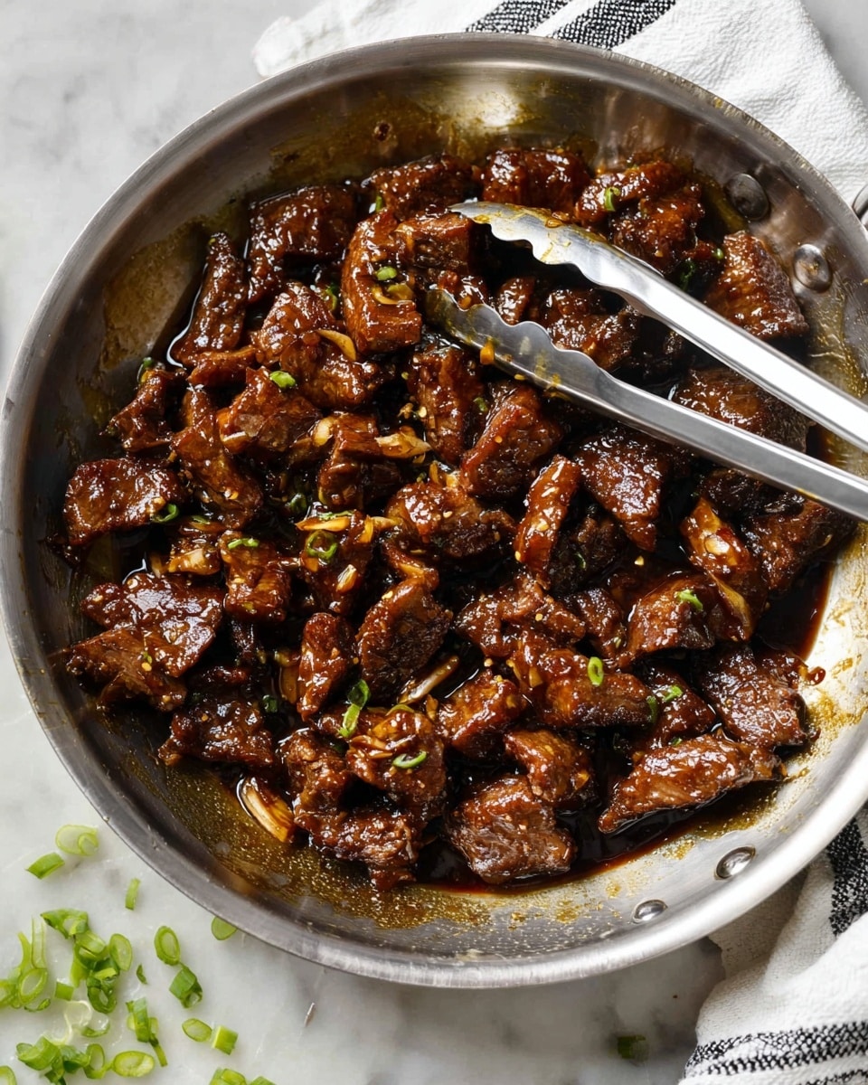 In a shiny stainless steel pan, there is a dish made of many small pieces of dark brown cooked meat covered in a thick glossy sauce with a slightly sticky texture. The meat looks tender with caramelized edges and some chopped garlic visible in the sauce. A pair of metal tongs rest inside the pan, partially dipped in the meat mixture. Around the pan, there is a white marbled surface with some small chopped green onions scattered near the bottom edge. A white cloth with black stripes is placed at the top right corner of the image. Photo taken with an iphone --ar 4:5 --v 7