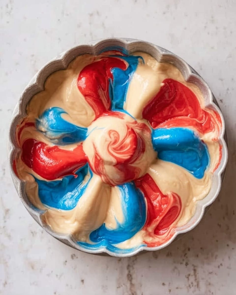 A round bundt pan filled with batter in three colors, cream, bright red, and bright blue. The batter is poured in random swirls and patches, mostly cream with bold streaks of red and blue spread throughout. The pan's fluted edges create a flower-like shape around the batter, and the pan itself is white. The whole scene sits on a white marbled surface. photo taken with an iphone --ar 4:5 --v 7