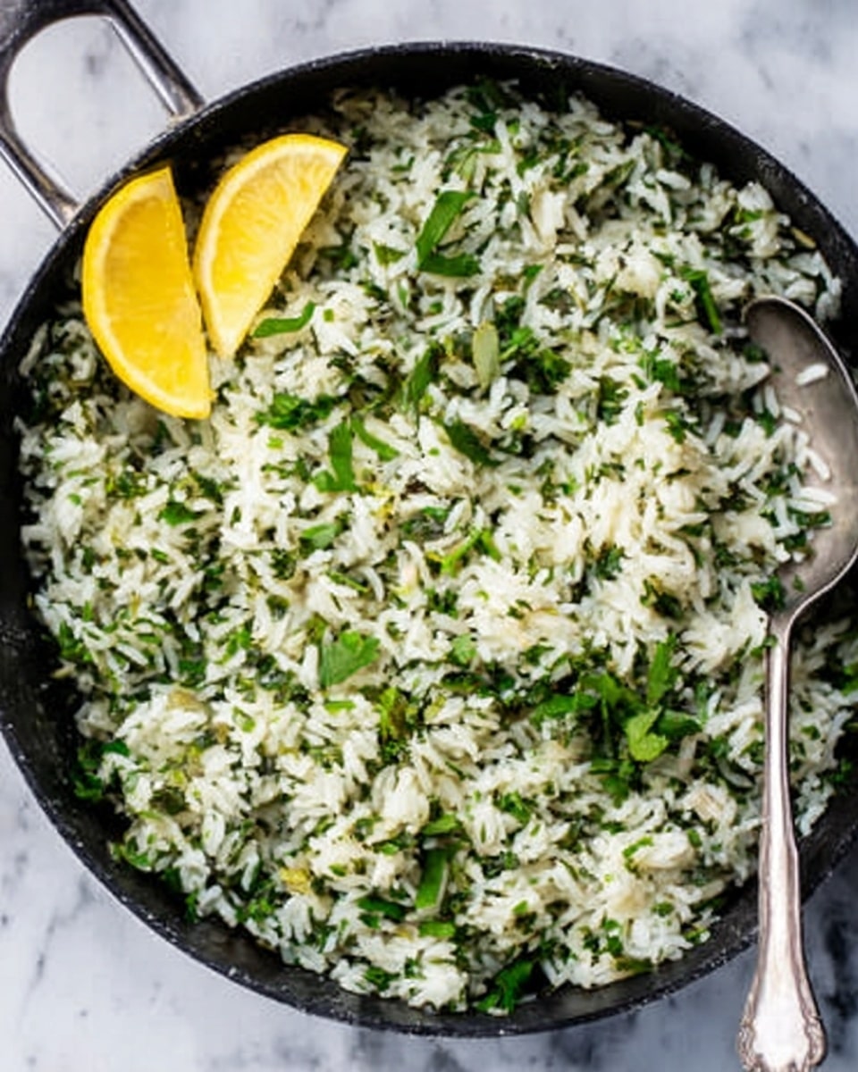 A close-up image of a black pan filled with cooked rice mixed with finely chopped green herbs. The rice is white with a light, fluffy texture, evenly blended with small pieces of darker green leaves scattered throughout. Two lemon wedges are placed on the top left side of the pan, adding bright yellow color contrast. A silver spoon is placed on the right edge of the pan, partially resting inside the rice. The pan is set on a white marbled surface. photo taken with an iphone --ar 4:5 --v 7