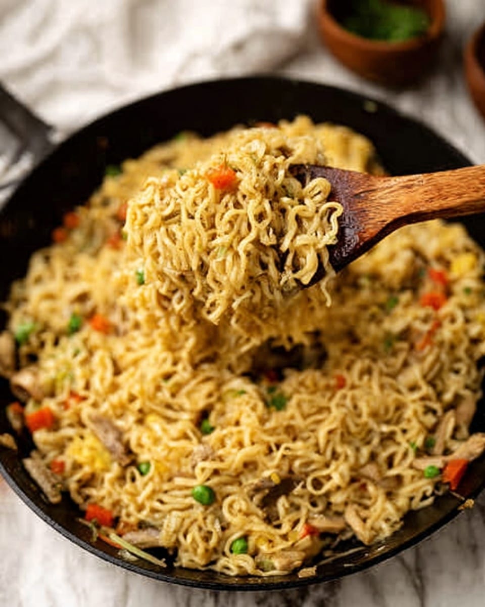 The image shows a black pan filled with cooked noodles mixed with small pieces of vegetables like carrots and green peas. A wooden spatula is lifting a portion of the noodles, showing their curly texture and the mix of colorful veggies inside. The noodles look soft and shiny, with a slight golden color. The background features some white marbled texture with a white cloth and a small brown bowl partially visible. The focus is on the lifted noodles and the pan below. Photo taken with an iphone --ar 4:5 --v 7