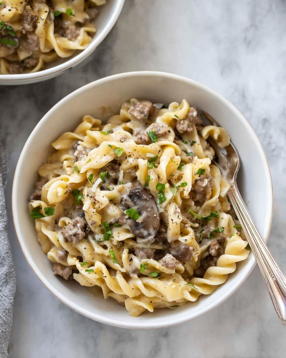 The image shows a large silver pot filled with a creamy pasta dish. The pasta is curly and pale yellow, mixed with small pieces of browned meat and darker bits that look like mushrooms, all coated in a thick light beige sauce. There are small green herb sprinkles on top, adding a touch of color. A wooden spoon is lifting a portion of the pasta from the pot, showing the thick texture and ingredients mixed together well. The pot sits on a white marbled surface. Photo taken with an iphone --ar 4:5 --v 7