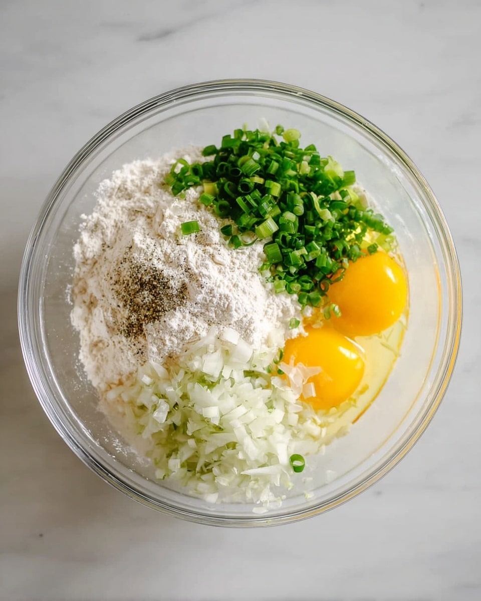 A clear glass bowl on a white marbled surface contains several ingredients layered separately. On one side, there is a mound of white flour with a sprinkle of black pepper on top. Next to it, finely chopped white onions form a small pile. Bright green chopped scallions are placed on another side, adding a fresh color contrast. Two raw eggs, with vibrant yellow yolks and clear whites, are positioned together in the bowl, opposite the scallions. The ingredients are evenly spaced and clearly visible in the transparent bowl. Photo taken with an iphone --ar 4:5 --v 7