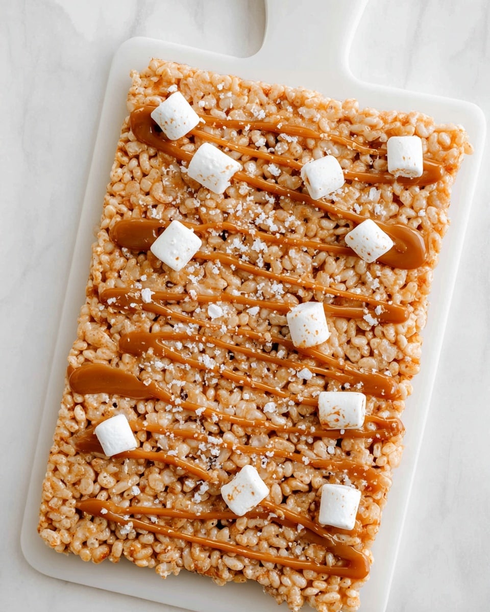 The image shows one thick, rectangular bar of light golden brown cereal treats placed on a white board with a handle at the top. The bar has a rough texture made from puffed rice cereal tightly pressed together. Drizzled across the top in thin lines and dollops is a smooth caramel-colored sauce that adds shine and contrast. Small, white, soft marshmallow pieces are scattered evenly across the surface. There are also small shiny white flakes sprinkled on the bar, adding extra texture. The background is a white marbled surface. photo taken with an iphone --ar 4:5 --v 7