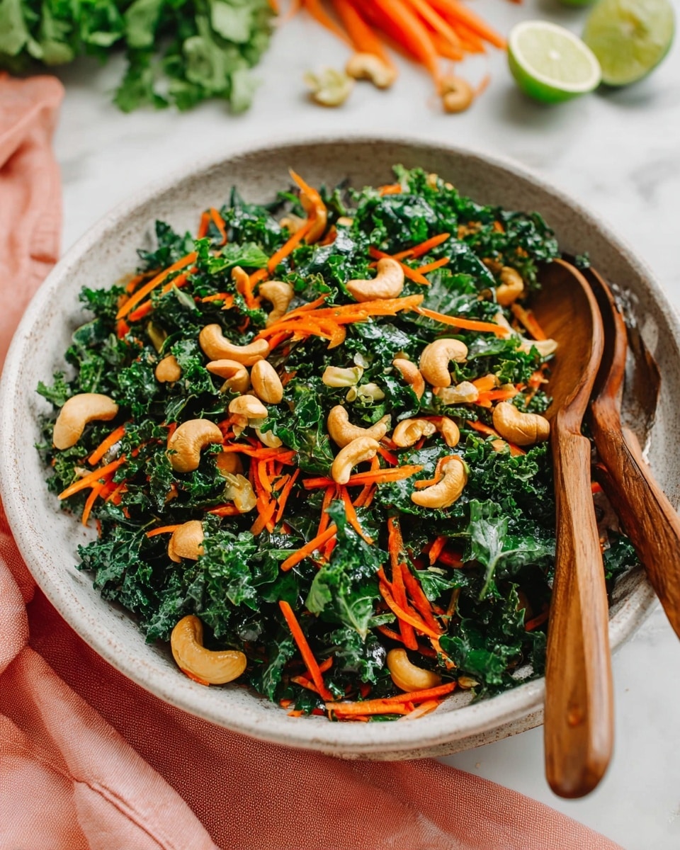 A white textured bowl holds a fresh salad with two main layers: the bottom layer is dark green curly kale leaves with a rough texture and a slight shine; mixed in are thin bright orange shredded carrot strips spread evenly on top and throughout the kale. Scattered on the salad are light brown whole cashew nuts adding smooth curves. Two wooden utensils rest along the edge of the bowl on the right side. The bowl sits on a white marbled surface with a soft pink cloth folded nearby and blurred ingredients like lime halves, carrots, and leafy greens in the background. Photo taken with an iphone --ar 4:5 --v 7
