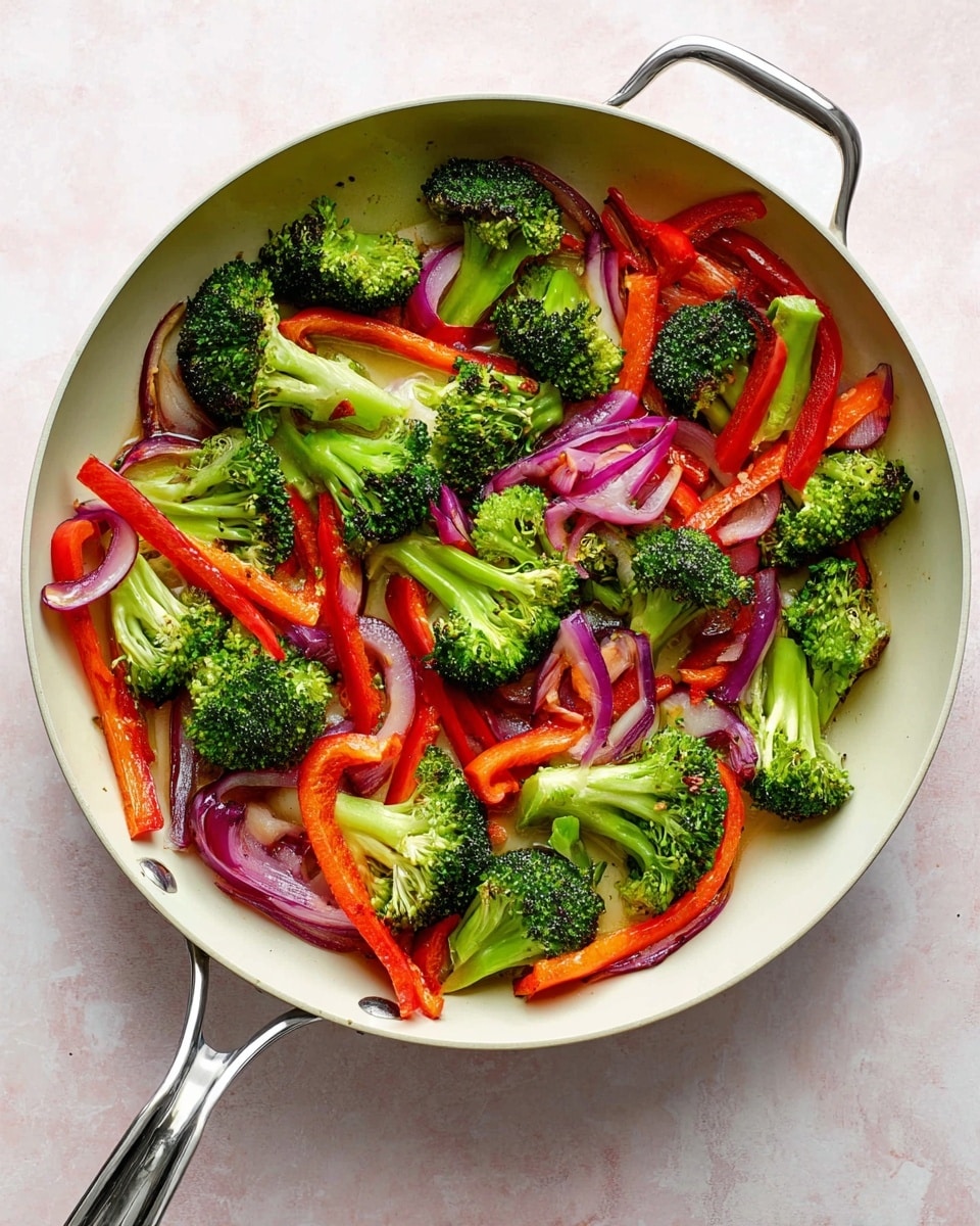 A white pan filled with cooked vegetables including bright green broccoli florets scattered all around, thin long strips of red bell pepper layered among the broccoli, and slices of purple onion mixed throughout. The vegetables are spread evenly in the pan showing a mix of vibrant red, green, and purple colors with some light browning on the onions. The pan is placed on a white marbled surface. photo taken with an iphone --ar 4:5 --v 7