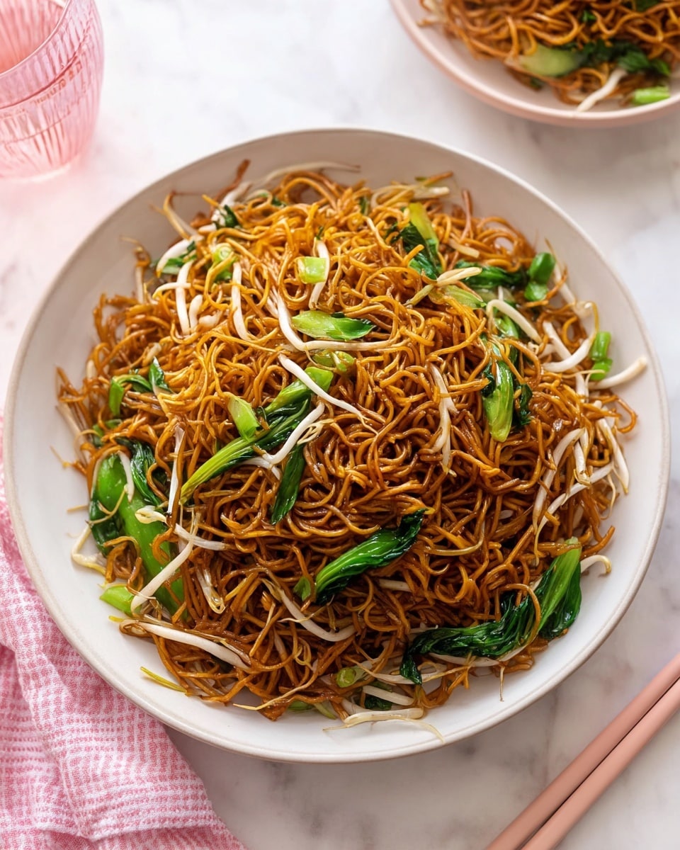 A white shallow bowl filled with thin, dark brown fried noodles mixed with light green leafy vegetables and thin white bean sprouts scattered throughout. The noodles are slightly shiny and tangled, with the vegetables adding freshness and contrast. The bowl sits on a white marbled surface with a pair of light pink chopsticks placed on the upper right side. A pink glass with some water is partially visible on the left. The scene is bright and clean with a soft pink checkered cloth in the bottom left corner. Photo taken with an iphone --ar 4:5 --v 7