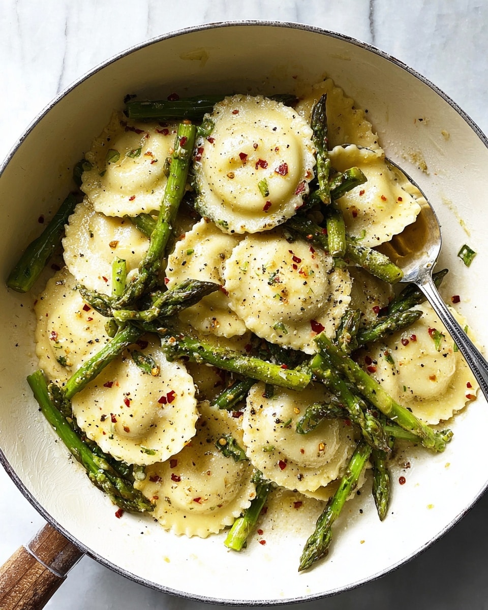 A white pan filled with round ravioli pasta, each piece pale yellow with a lightly textured edge and specks of black pepper and red chili flakes on top. Mixed in and layered between the ravioli are bright green asparagus spears, showing some grill marks and a slightly shiny surface from light oil. The dish is served on a white marbled surface, with a silver spoon resting inside the pan among the ravioli and asparagus. The lighting highlights the soft texture and glossiness of the ravioli and vegetables. photo taken with an iphone --ar 4:5 --v 7