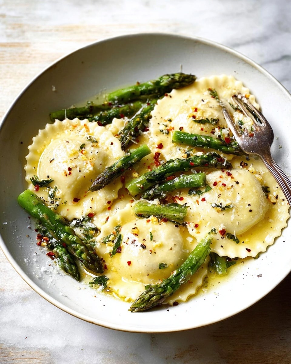 In a shallow white bowl on a white marbled surface, there are six round ravioli with scalloped edges scattered across the plate. The ravioli are pale yellow and topped with a light sprinkling of cracked black pepper and red chili flakes. Bright green asparagus spears are placed between the ravioli, some whole and some slightly angled, adding texture and color contrast. A silver fork is resting at the edge of the bowl, partially touching the ravioli and asparagus. The dish has a light olive oil or butter glaze that gives a slight shine to the ravioli and asparagus. photo taken with an iphone --ar 4:5 --v 7