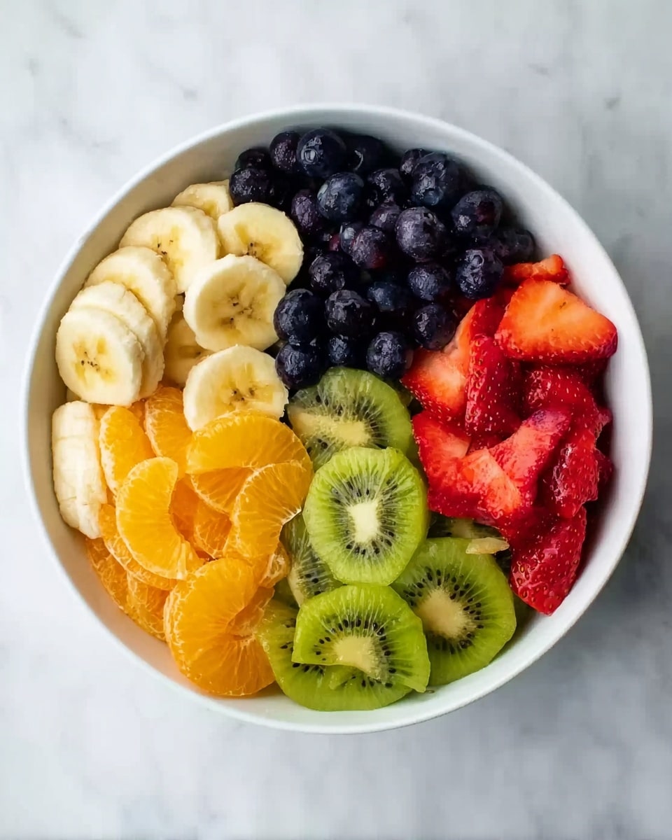 A white bowl filled with five different sliced fruits arranged in separate sections. One section has light yellow banana slices, another has deep blue blueberries, the third holds bright green kiwi slices with the peel partially visible, the fourth has bright orange mandarin segments, and the fifth section contains red strawberry slices. The bowl is placed on a white marbled surface. The colors are vivid and the fruit textures vary from smooth banana to juicy strawberries and soft blueberries, showing freshness. photo taken with an iphone --ar 4:5 --v 7