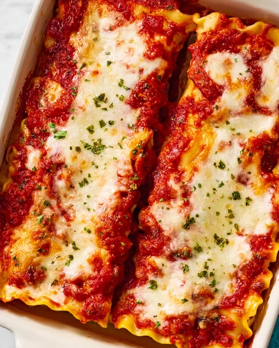 The image shows two rolled lasagna pieces in a white baking dish. Each roll has visible layers of soft pasta sheets filled with a rich, red tomato sauce and melted white cheese on top. The cheese is slightly browned and bubbly with small green herb sprinkles scattered over the sauce and cheese. The edges of the lasagna rolls are slightly browned from baking, and the white marbled surface around the dish adds a clean and bright background. Photo taken with an iphone --ar 4:5 --v 7