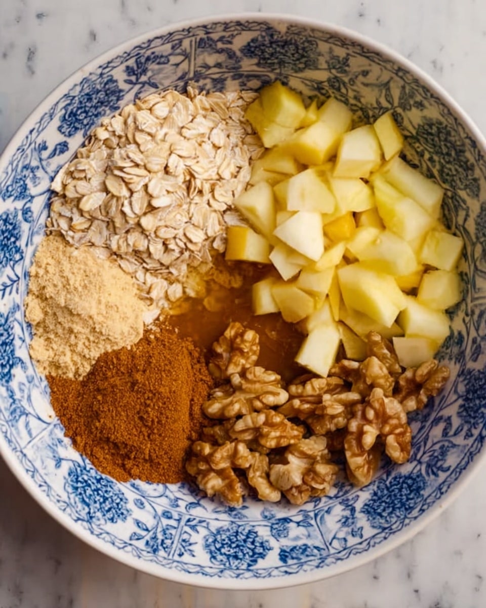 A white bowl with a blue floral pattern contains seven distinct sections of ingredients placed side by side. Starting from the top left moving clockwise: a cluster of light brown rolled oats, a dark golden liquid resembling honey covering part of the oats, small yellowish cubes of chopped apple, a pile of walnut halves with a rough texture, a cinnamon powder mound with a reddish-brown color, and a small clump of light brown flakes on the left edge. The bowl is set on a white marbled surface. photo taken with an iphone --ar 4:5 --v 7