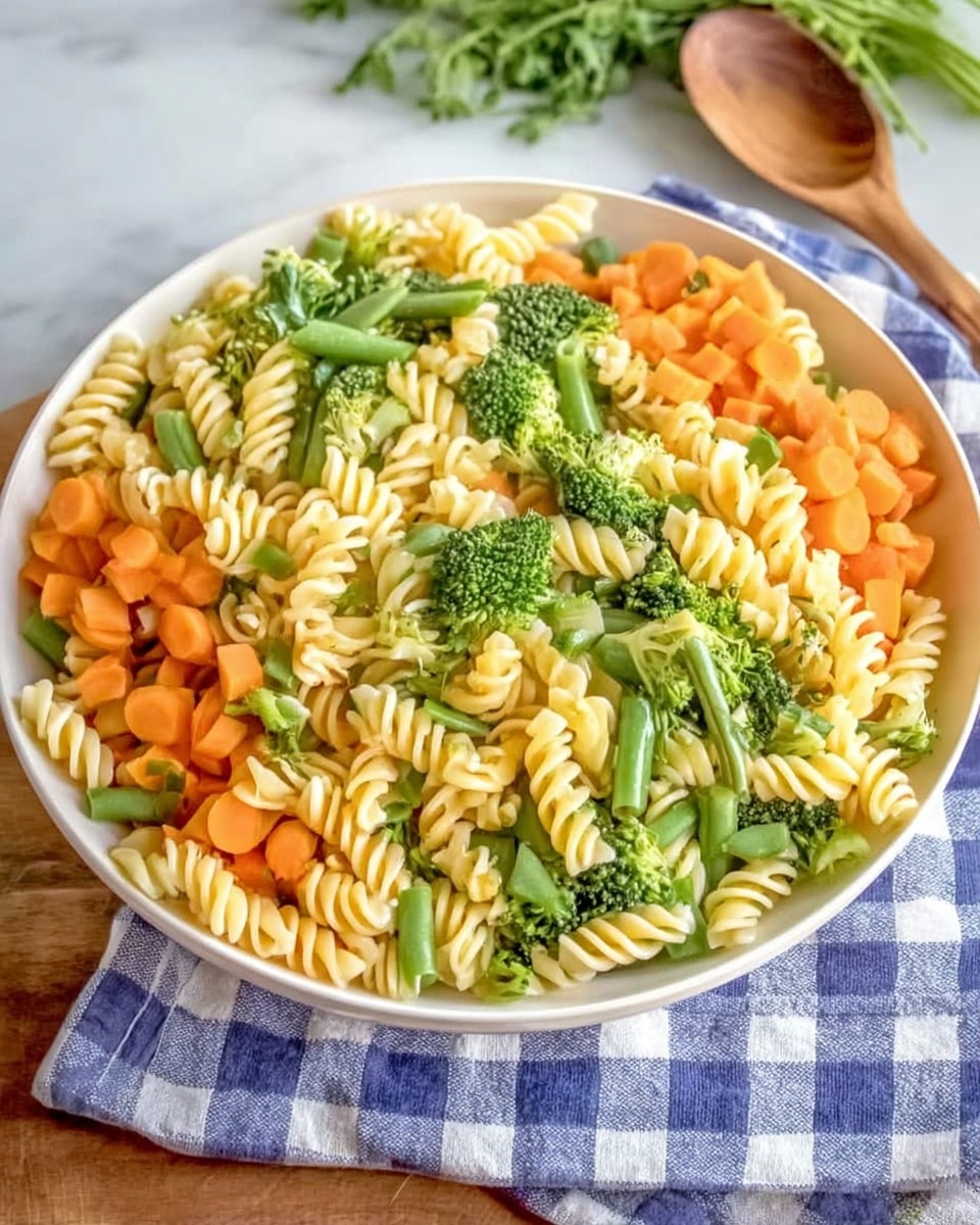 A white plate filled with a colorful pasta salad, featuring three main layers: the bottom has twisted rotini pasta in pale yellow and light green shades, the middle layer has bright green broccoli florets and sliced green beans, and the top layer shows thin, smooth orange carrot slices scattered evenly. The plate sits on a white marbled surface with a blue and white checkered cloth partially visible underneath. A wooden spoon is just above the plate and some green leafy herbs are in the background. Photo taken with an iphone --ar 4:5 --v 7