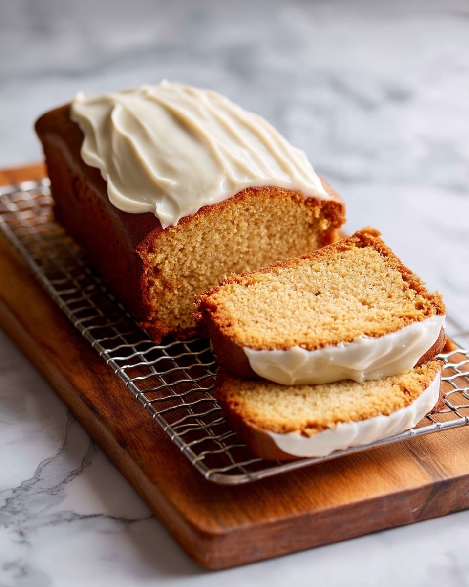 A loaf of brown cake with a thick layer of creamy white frosting on top, sitting on a metal cooling rack placed over a wooden board. Two slices of the cake lie next to the loaf, showing the pale brown inside and the white frosting spread evenly on top of each slice. The background and surface have a white marbled texture. Photo taken with an iphone --ar 4:5 --v 7