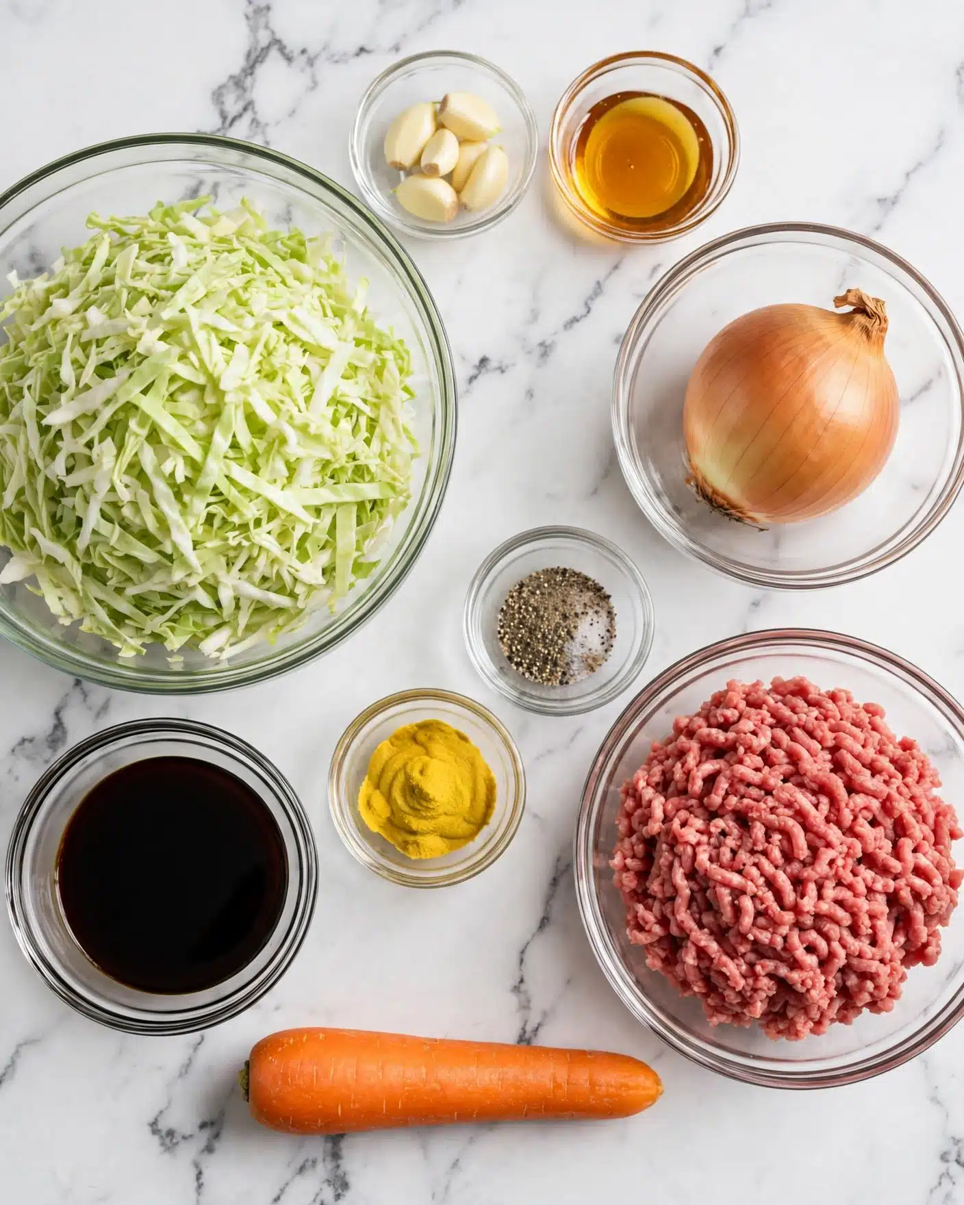 Egg Roll in a Bowl Recipe 4 The image shows a white marbled surface with ingredients arranged neatly. A large clear bowl on the left holds finely shredded green cabbage. Below it, a small round clear bowl contains dark soy sauce. A single whole orange carrot lies horizontally at the bottom center. On the right side, a clear bowl has raw ground meat with a reddish color and fine texture. Above the carrot is a small clear bowl with yellow mustard powder, next to a small bowl of ground black pepper mixed with salt. A medium clear bowl at the top right holds a whole yellow onion. Above the carrot, centered along the top row, are two very small clear bowls, one containing light yellow garlic cloves and the other with a golden liquid, likely honey or oil. The whole scene is bright and clean, organized by size and color. Photo taken with an iphone --ar 4:5 --v 7