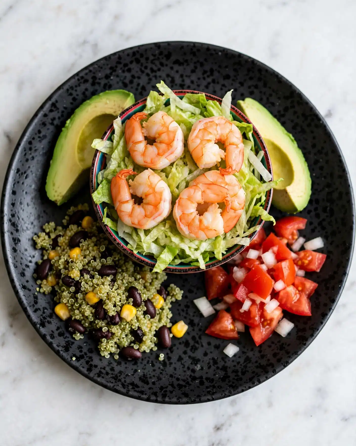 Avocado Shrimp Quinoa Bowl with Cilantro Vinaigrette Recipe 5 A dark speckled plate holds a colorful shrimp salad with five grilled shrimp placed near the center. Under and around the shrimp are three avocado slices, bright green in color. To the right and left edges is shredded pale yellow and light green lettuce. Below the shrimp is green quinoa mixed with black beans and small yellow corn pieces. Near the bottom edge is a small portion of red diced tomatoes mixed with white onions. The plate rests on a white marbled surface photo taken with an iphone --ar 4:5 --v 7