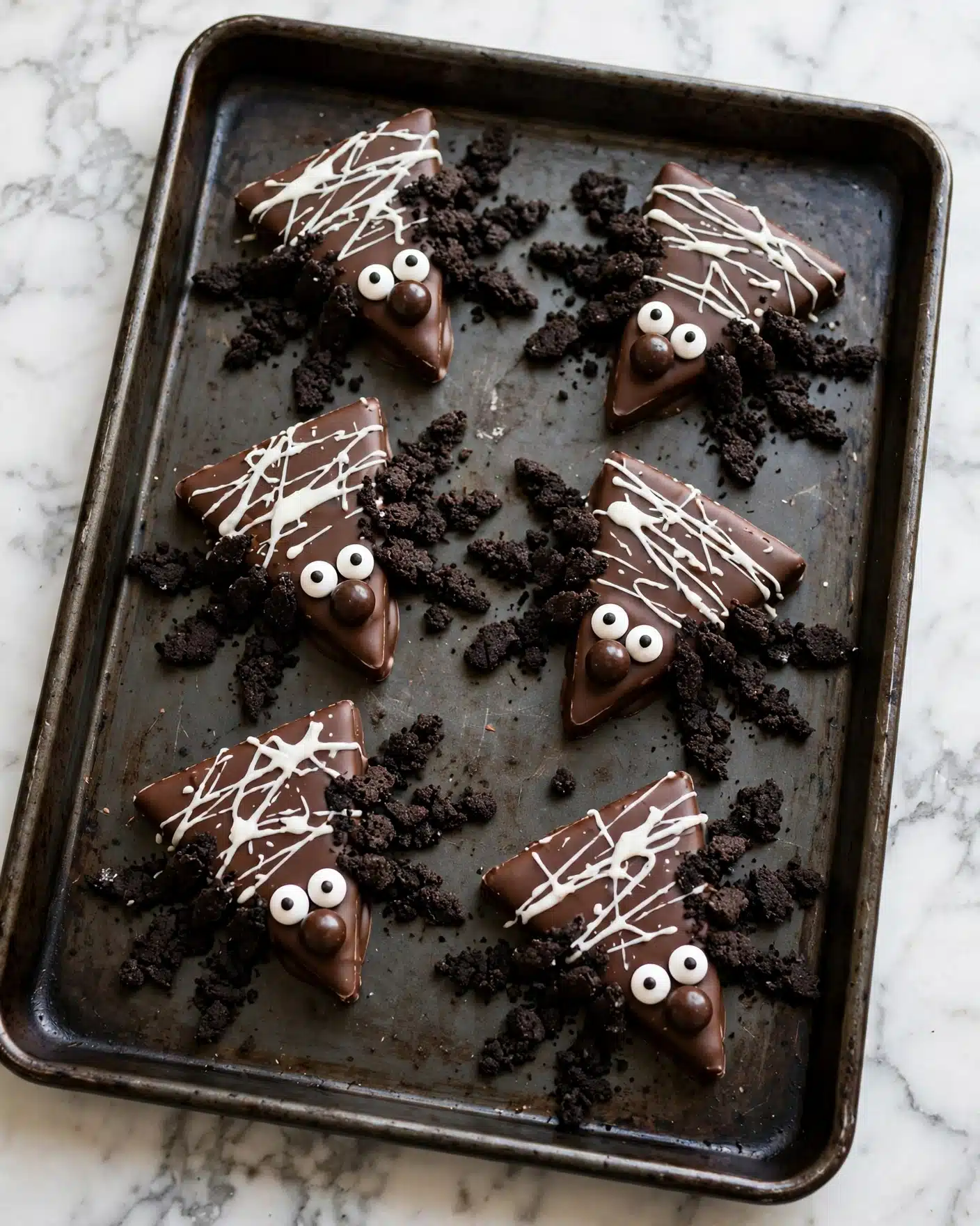Black Widow Peanut Butter Bars Recipe 5 A large rectangular chocolate base is topped with thin, irregular white chocolate drizzles crisscrossing across the entire surface like a spider web. On top of the chocolate layer, multiple small spider figures are placed, each made of round brown chocolate balls for bodies, decorated with white candy eyes featuring black pupils, and black textured candy pieces forming the legs and heads. The chocolate base rests on a dark metal tray with a few small, orange decorative pumpkins around the edges, all set against a white marbled surface. photo taken with an iphone --ar 4:5 --v 7