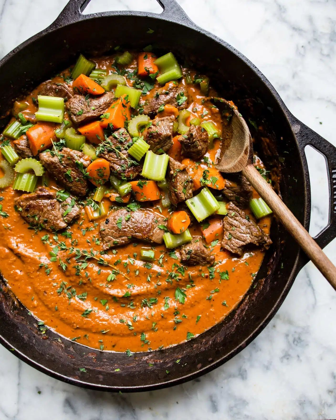 Life Changing Instant Pot Beef Stew Recipe 5 A dark pan filled with stew shows three main layers: a thick orange sauce spread evenly at the bottom, pieces of brown meat scattered on top, and bright orange carrot chunks and light green celery pieces spread throughout. The dish is garnished with finely chopped green herbs, giving a fresh touch all over. A wooden spoon rests inside the pan, placed on the right side, with its handle stretching out over the white marbled surface. The pan itself has very dark edges that contrast with the bright colors inside. photo taken with an iphone --ar 4:5 --v 7